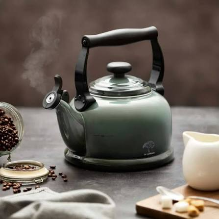 A sage green stovetop whistling kettle steaming beside a jar of coffee beans