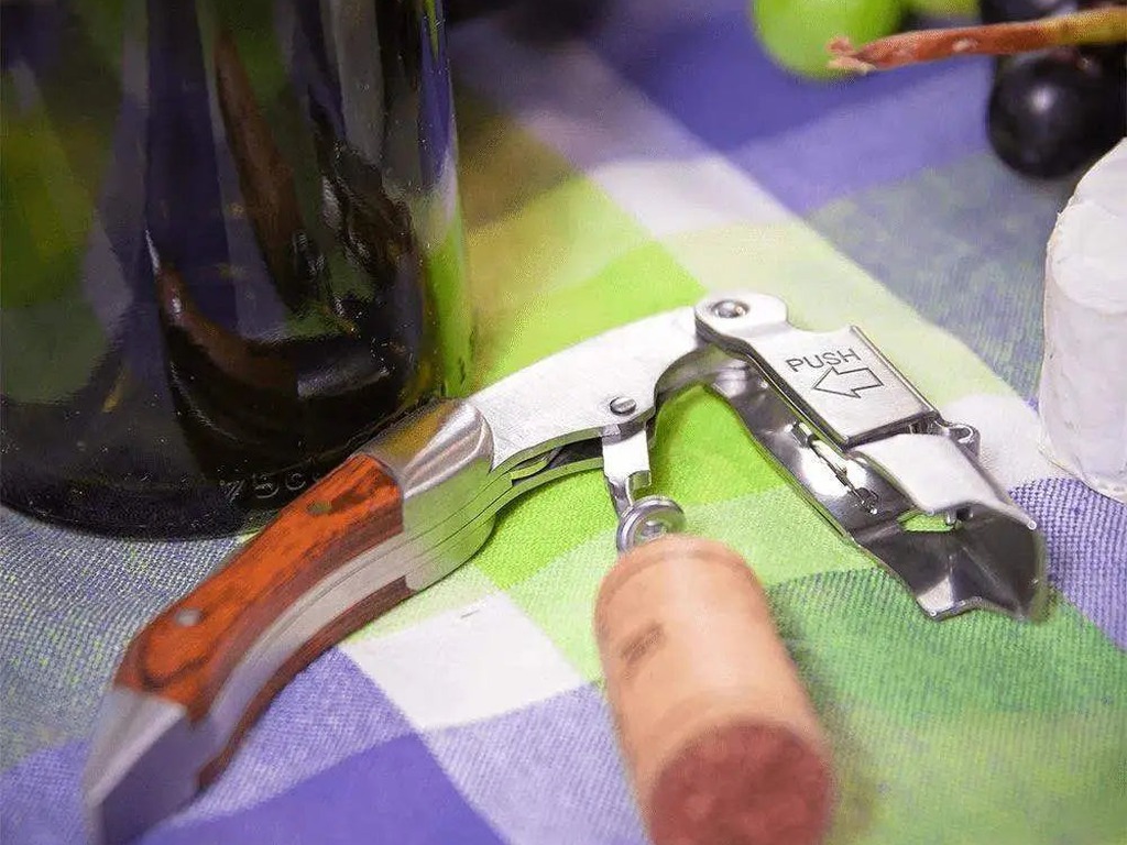 Cilio Waiter's Friend Legno corkscrew on a checked cloth beside a wine bottle, cork and grapes