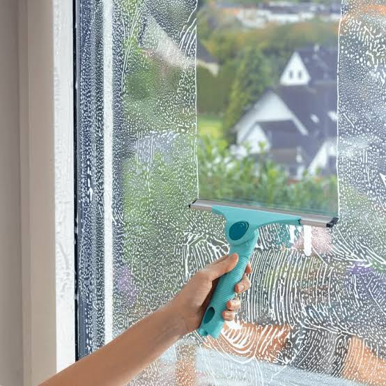 A hand drawing a turquoise squeegee window wiper down a soapy kitchen window pane
