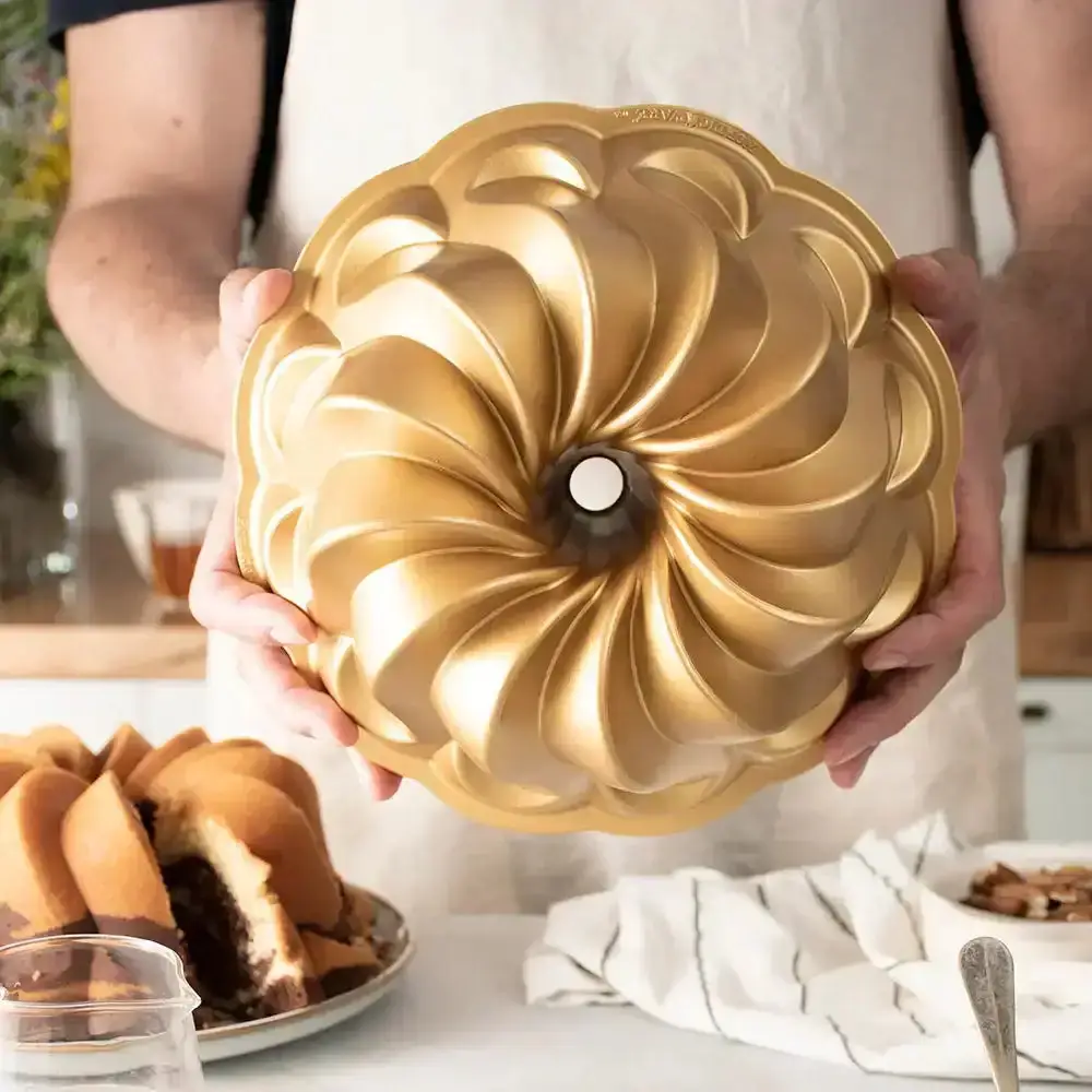 A baker holding a gold fluted bundt tin above a sliced marble bundt cake