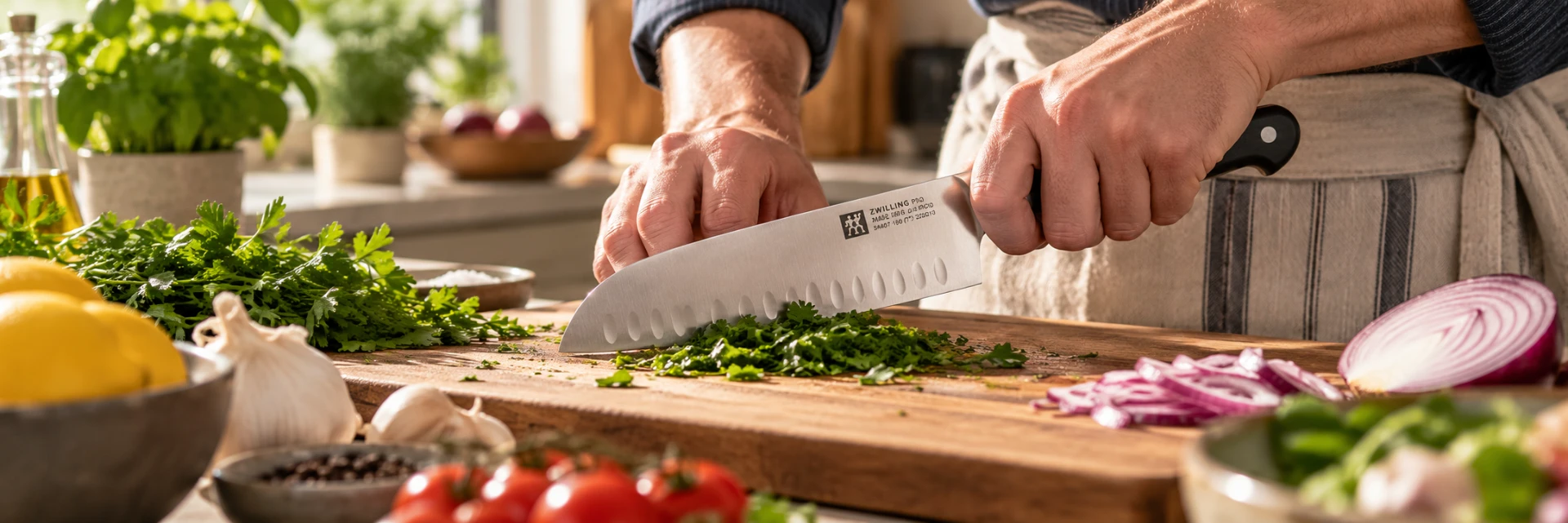 Hands chopping fresh herbs with a santoku kitchen knife on a wooden cutting board.