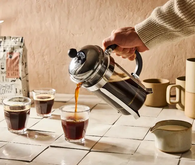 A stainless French press being poured into small glasses of freshly brewed filter coffee
