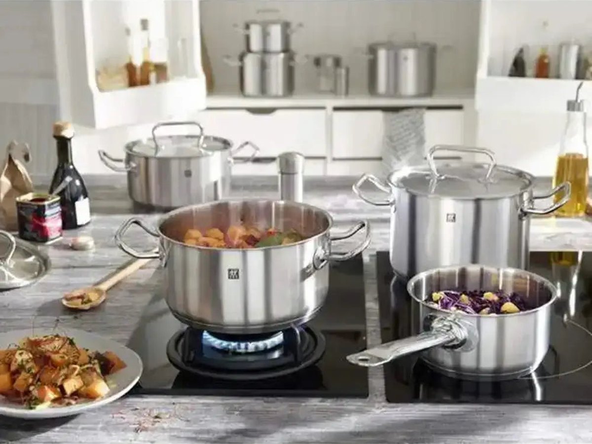 A matching stainless steel pot set in use on a hob in a bright white kitchen