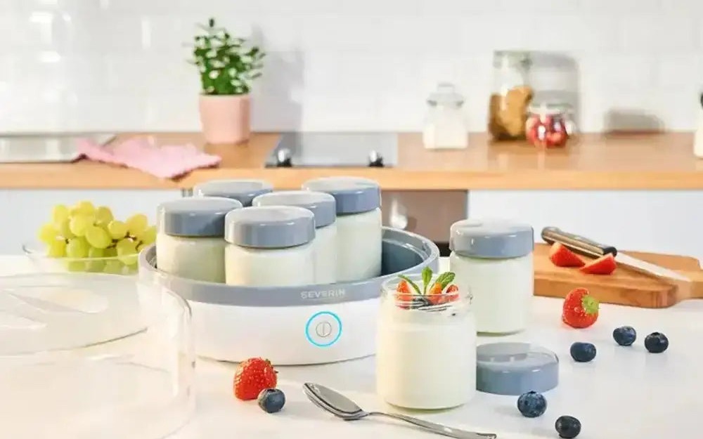 A Severin yoghurt maker with glass jars of set yoghurt and fresh berries on a kitchen table