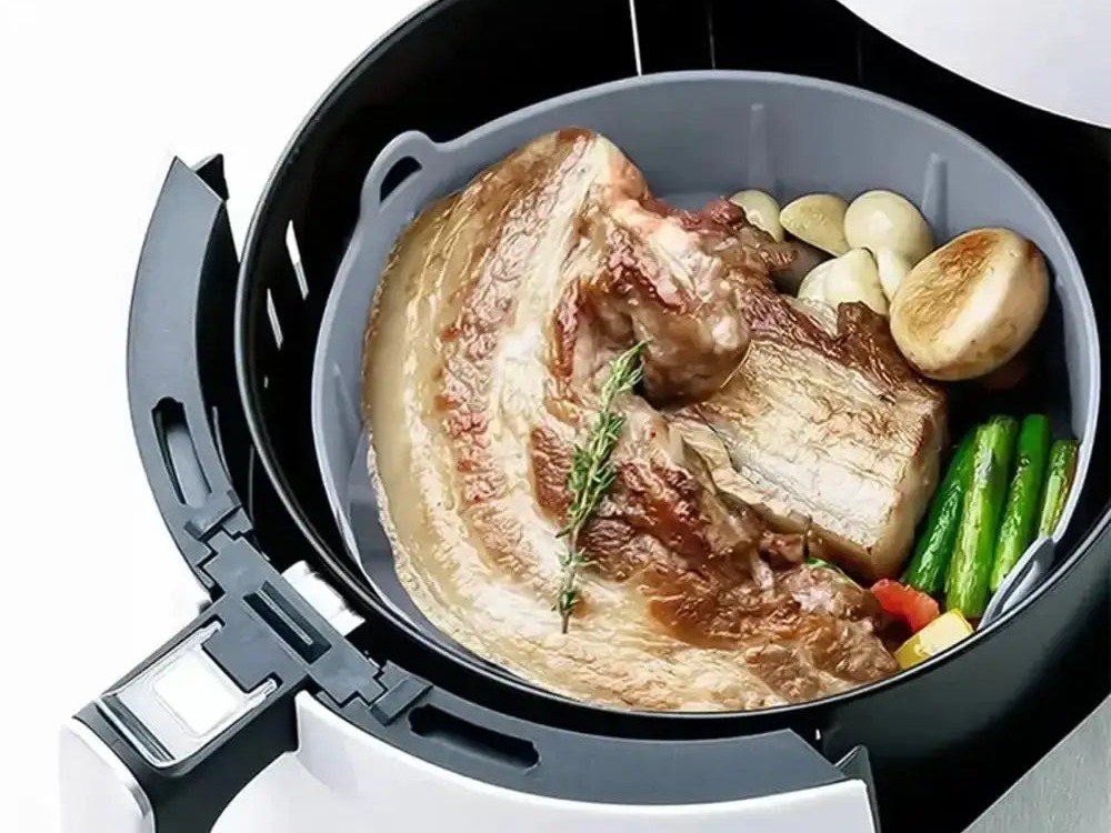 Pork belly and vegetables roasting in a silicone air fryer basket liner