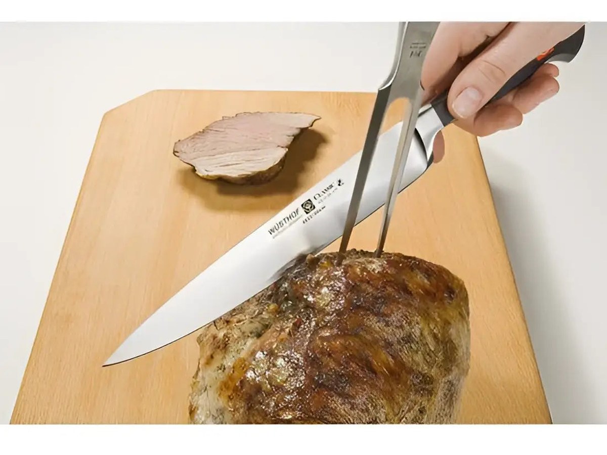 A carving knife slicing a rested roast joint on a wooden board