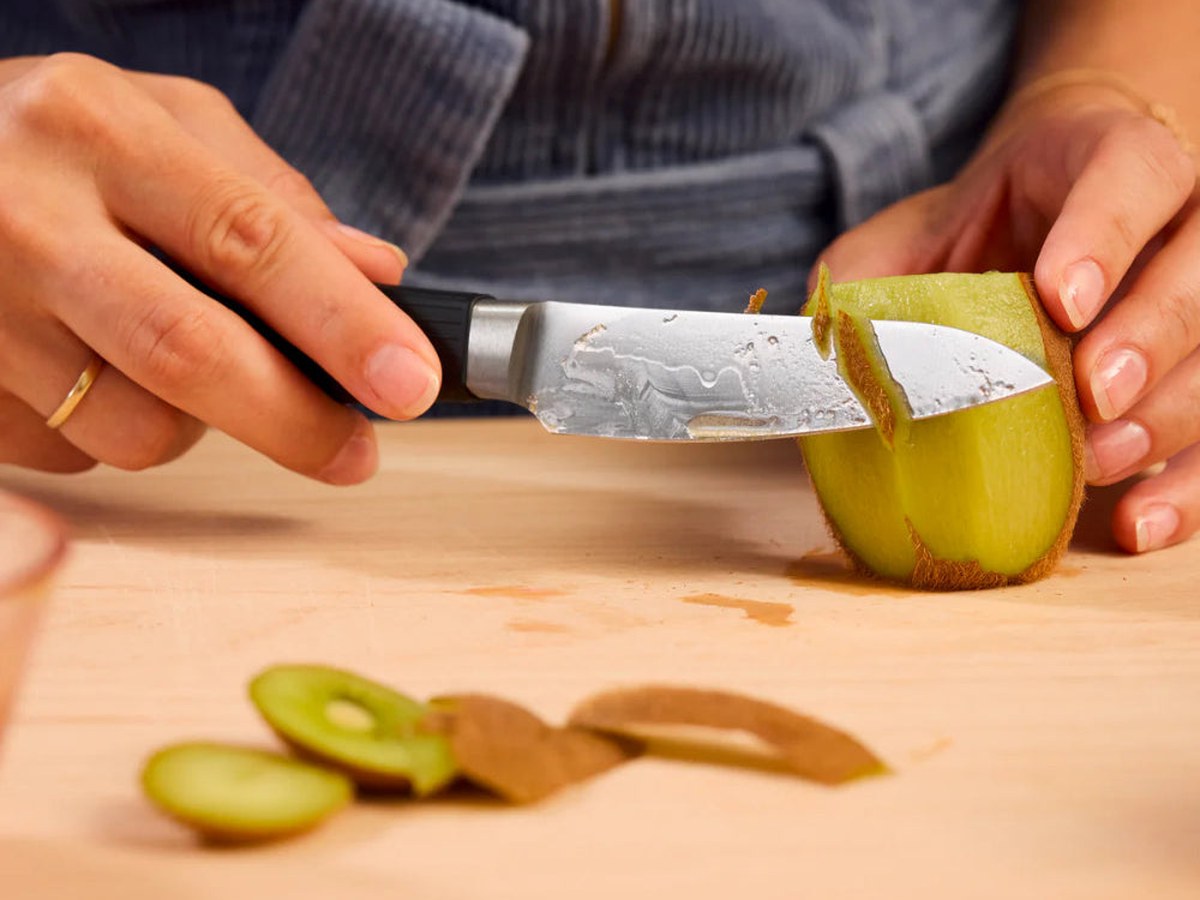 A paring knife trimming fruit held in the hand over a kitchen counter