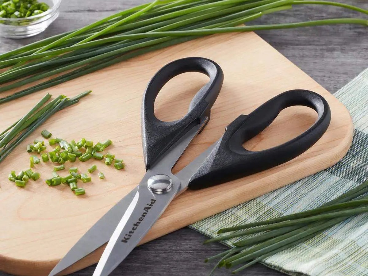Hands snipping fresh chives with kitchen scissors over a ceramic bowl