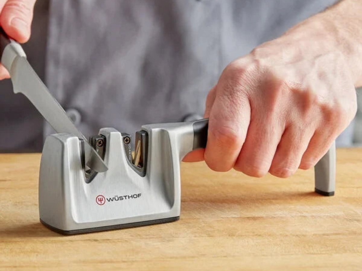A kitchen knife being drawn through a countertop sharpener on a wooden board