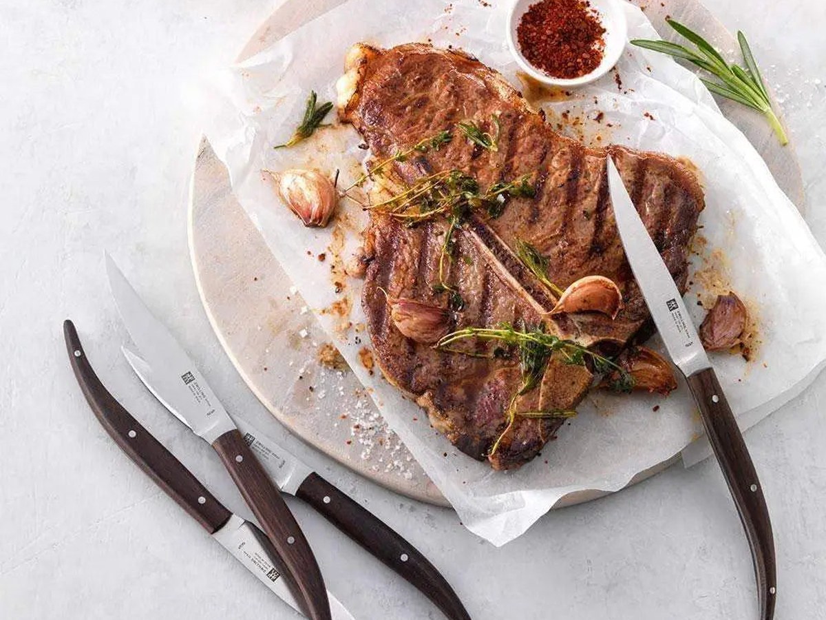 Steak knives resting on a linen napkin beside a rested steak on a wooden board