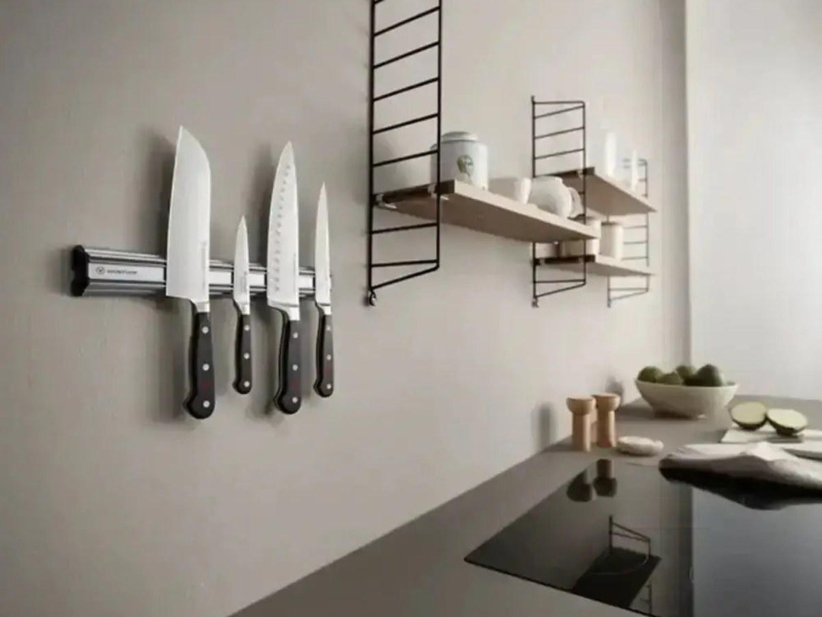 A hand returning a knife to a wooden knife block beside a magnetic wall strip