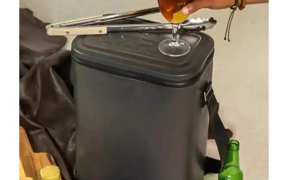 A drink being poured beside a Lizzard charcoal insulated cooler bag outdoors