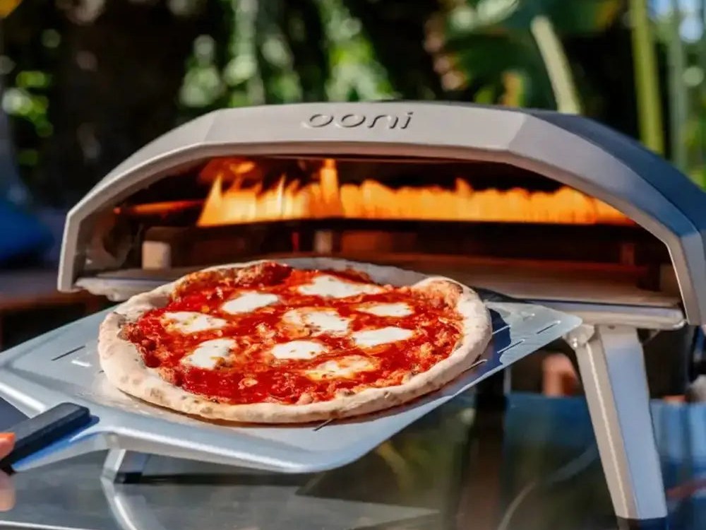 A margherita pizza on a peel in front of a lit Ooni Koda 16 gas pizza oven