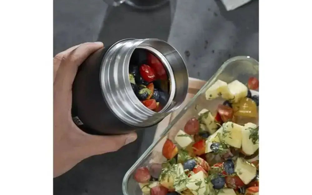 A hand holding an open Zwilling Thermo insulated travel food jar filled with salad