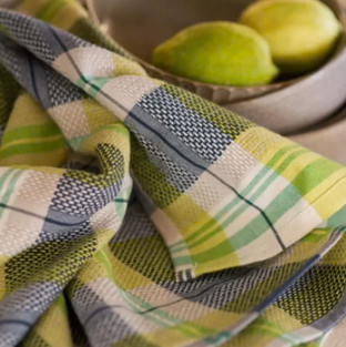 Close-up of draped green, yellow, grey and white checked tea towels with lemons in a bowl behind